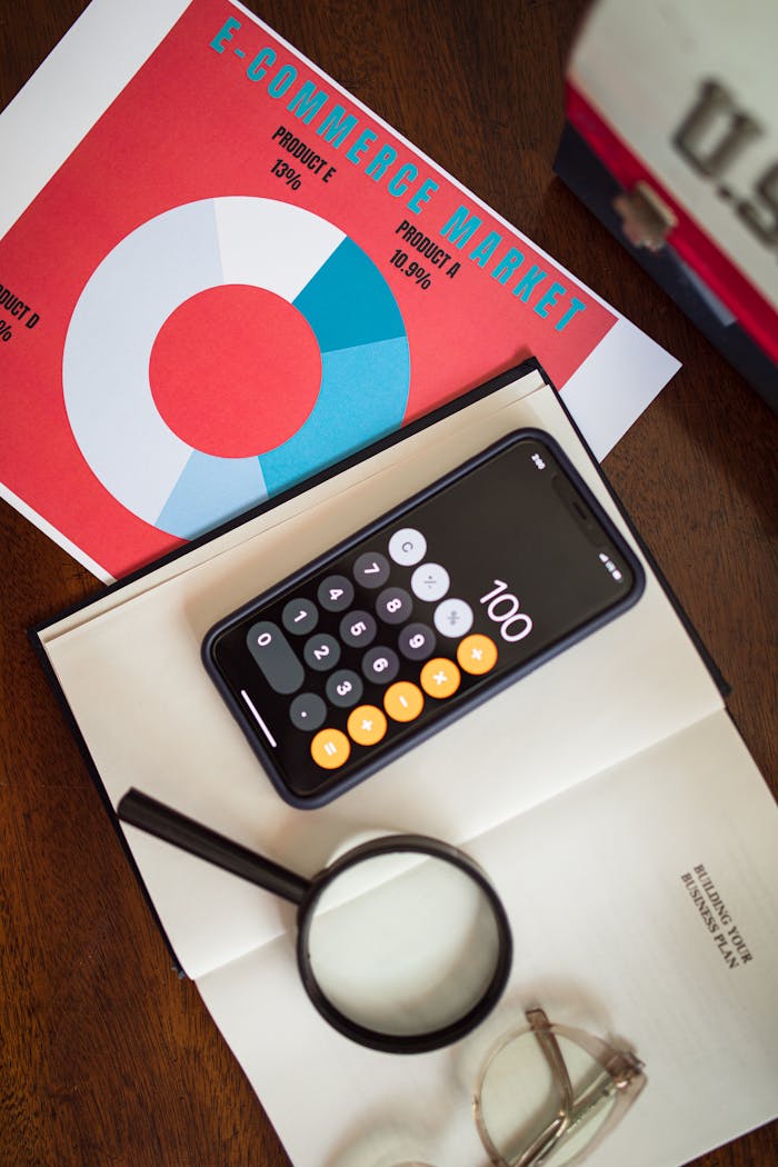 Overhead view of e-commerce chart with smartphone calculator and magnifying glass on a table.